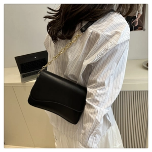 Minimalistische schwarze Umhängetasche mit goldener Kette am Model im Büro getragen