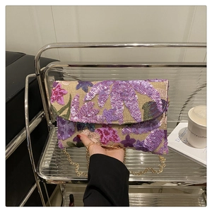 Detail van bloemenborduurwerk met pailletten op een geweven tas met gouden ketting