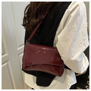 Macro view of burgundy patent leather shoulder bag with glossy finish and flap design