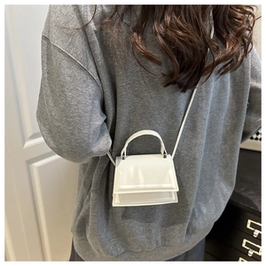 Mini white leather handbag with oversized curved handle shown as a crossbody on a model