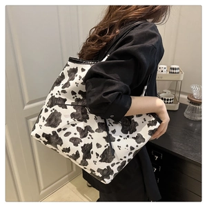 Detail view of large cow print tote bag with black straps worn over the shoulder