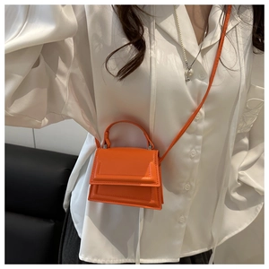 Detail of bright orange micro handbag featuring iconic curved handle and leather texture