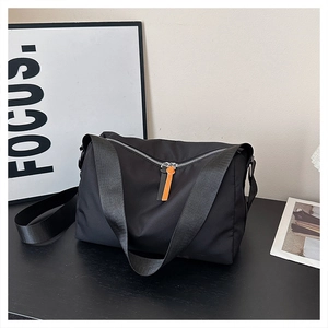 Detail of black nylon crossbody bag with dual-tone orange and black leather zipper pull