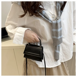 Detail view of mini black matte leather handbag with fine stitching and slim shoulder strap