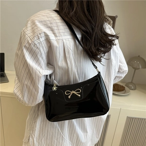 Glossy black underarm bag with gold bow clasp worn by a model in a minimalist setting