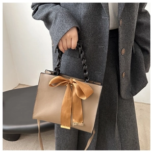 Detail of hand-woven black handle and orange silk bow on khaki PU leather crossbody bag