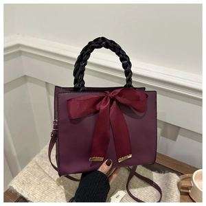 Detail of burgundy handbag with black woven handle and large silk bow decoration