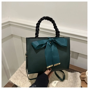 Close-up of dark green PU leather handbag with blue silk bow and woven handle detail