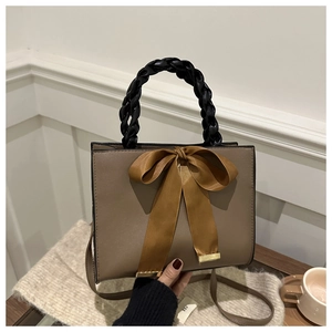 Elegant khaki handbag with brown silk bow and black woven handle on a cozy knit blanket