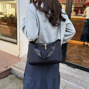 Sac bandoulière noir en tissu Oxford avec tirette orange, porté par un mannequin chic