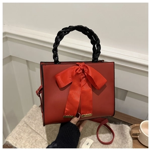 Detail of red square handbag featuring large silk bow and black woven handle with hand
