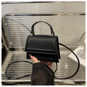 Detail of minimalist black matte leather small square bag with top handle and shoulder strap