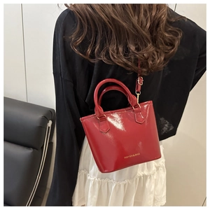 Détail du sac seau en cuir verni rouge avec lettrage doré et finition miroir polie
