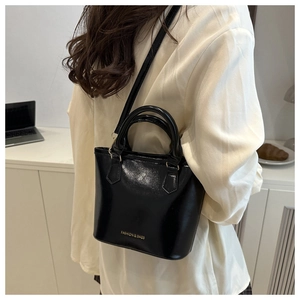 Gros plan du sac seau en cuir verni noir avec poignée supérieure et bandoulière réglable