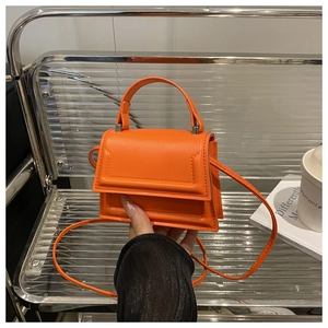 Detail of a vibrant orange mini crossbody bag with a top handle and silver hardware
