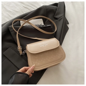 Detailed view of beige crossbody bag with quilted texture and gold lettering on flap