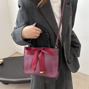 Burgundy PU leather handbag featuring a red satin bow and black woven handle design