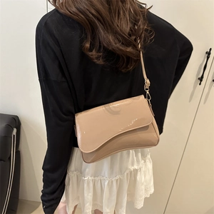 Glossy patent leather beige crossbody bag with curved flap shown on model back view