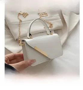 Close-up of white patent leather mini bag with gold chain strap and metal bar detail