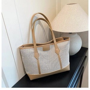 Detail of a large beige canvas tote bag with brown leather trim in a home setting