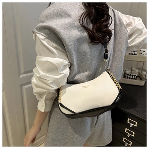 Close-up of contrast black and white pebbled leather bag on model with gold chain details