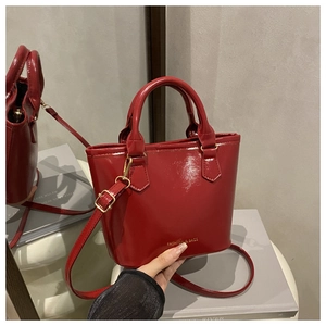 Détail macro du sac seau en cuir verni rouge avec boucles dorées et logo gravé