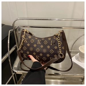Close-up of vintage monogram pattern with gold chain on dark brown baguette bag