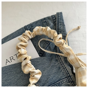 Detail of yellow checkered bag with pleated handle and silver zipper on denim backdrop