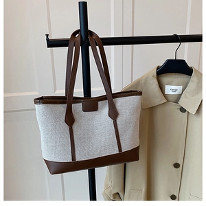Close-up of canvas tote bag with brown leather trim hanging on a black hanger