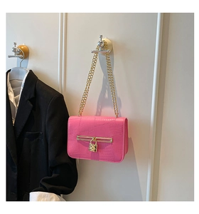 Detail of bright pink crossbody bag with crocodile texture and gold heart lock