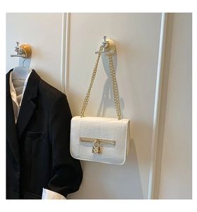 Close-up of white embossed leather handbag with gold heart lock and chain strap
