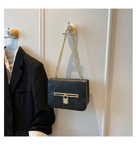 Close-up of black crocodile pattern shoulder bag with gold padlock and chain strap detail