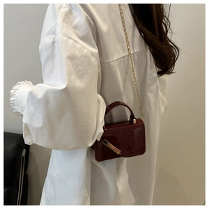 Detail of burgundy glossy mini bag with gold chain strap and metal bar decoration