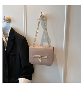 Detail of beige crocodile embossed leather bag with gold chain and metal lock pendant