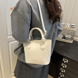 Sac seau en cuir blanc avec lettrage FASHION & BAGS porté par un mannequin en intérieur