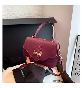 Detail of burgundy textured leather handbag with gold metal clasp and adjustable strap