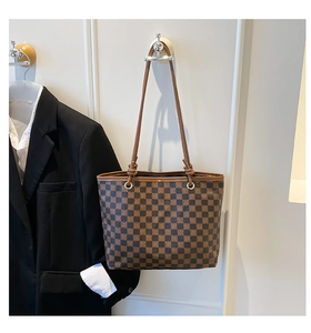 Detail of checkered tote bag with golden rings and thin brown leather handles