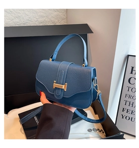 Detail of navy blue pebble leather bag with gold H-shaped clasp and detachable strap