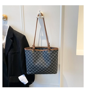 Detail of checkered tote bag showing brown leather handles and decorative knots
