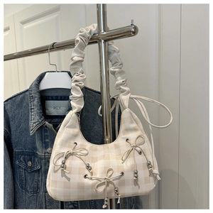 Detail of beige plaid crescent bag featuring pleated strap and bow accents with metal beads