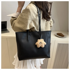 Detailed view of black leather tote bag with star plush charm on a model's shoulder