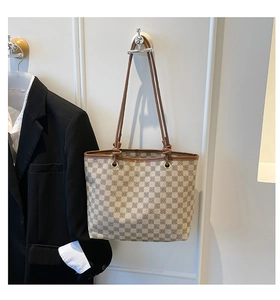 Detail of plaid tote bag with floral logo pattern and leather straps on office suit