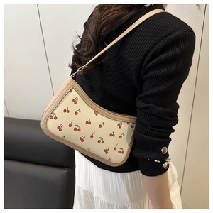 Close-up of cream underarm bag featuring red cherry prints and slim leather strap