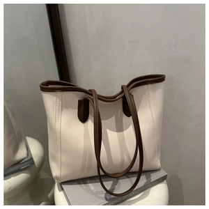 Close-up of minimalist cream tote bag with brown straps on an artistic white stool