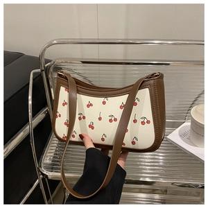 Detail of white shoulder bag featuring red cherry prints and dark brown leather straps