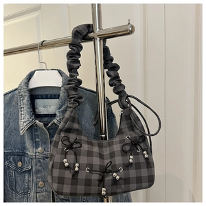Detail of grey plaid shoulder bag with ruched cloud strap and bow accents on denim jacket