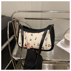 Detail view of cherry print shoulder bag with black strap on a minimalist shelf
