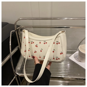 Detailed view of white leather shoulder bag featuring vibrant red cherry prints and slim strap