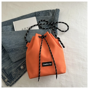 Détail macro du sac seau en nylon orange vif avec cordon à carreaux et écusson logo