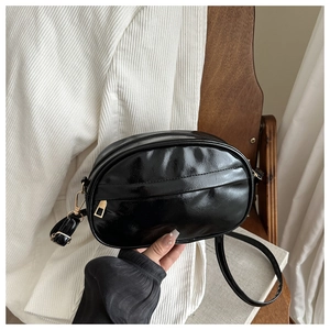 Detail of a black oval crossbody bag featuring glossy PU leather and gold-tone hardware